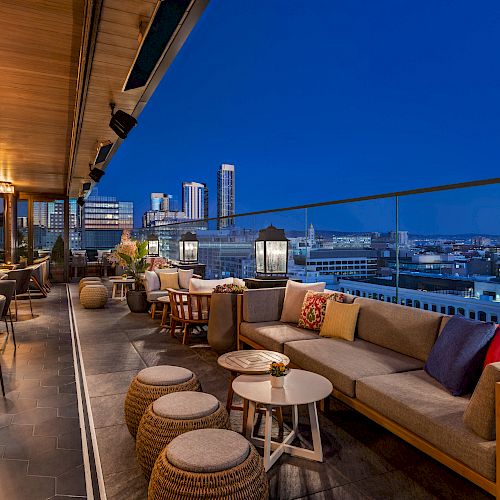 A stylish rooftop lounge with modern furniture, a city skyline view, cozy seating, and ambient lighting, perfect for dining or relaxing under the night sky.
